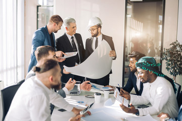 Interracial group of male architects and builders are engaged in lively discussion of the budget...