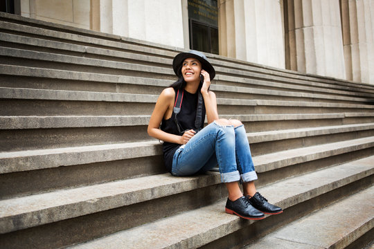 Female tourist wearing hat and denim jeans sitting on steps columns in background 