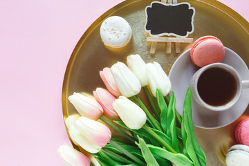 Obraz na płótnie Canvas Golden tray plate with macaroons, tulips, coffee cup on pink background. Close up. Decoration for Mothers day, International Women day, festive background.