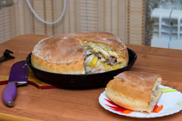 Kurnik, Russian meat pie. A traditional home-made pastry dish lies in a black pan on the table. Neer to a piece of pie on a plate. © PAVEL GERASIMENKO