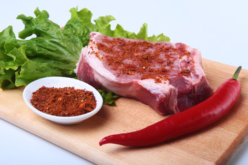 Raw pork steak with herbs, chili pepper and spices on cutting board. Ready for bbq.