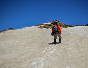 hombre adulto con mochila camina por la nieve hacia la cima de una montaña