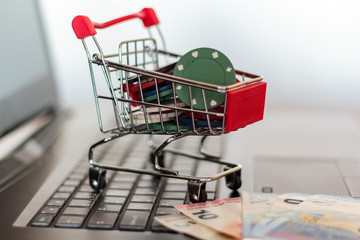Poker chips in a trolley and euro banknotes on a computer. Online Gambling addiction concept
