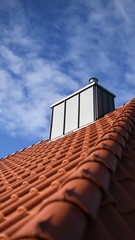 Ein rotes Hausdach des Dachdeckers mit Dachziegeln und ein neuer Schornstein oben vor dem blauen Himmel