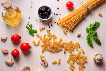 Top view flat lay of traditional ingredients for italian pasta on white table. Spaghetti, fusilli, tomatoes, green basil, olive oil, mushrooms and garlic