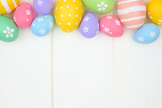 Colorful pastel Easter Egg top border against a white wood background. Top view with copy space.