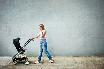Mother with baby girl (6-11 months) in stroller walking on sidewalk 