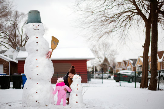 Mother and baby daughter (6-11 months) posing with big and small snowmen