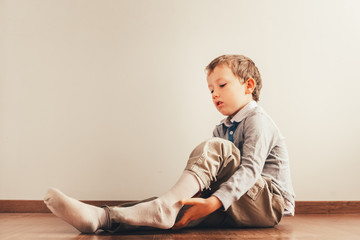 Naklejka premium Child with lots of independence sitting on the floor putting on his socks with an expression of effort