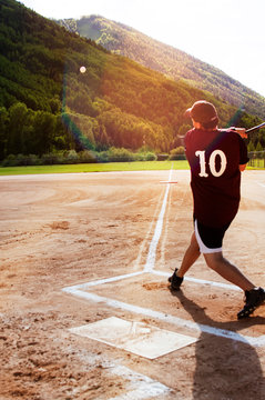 Softball player hitting ball in playing field 