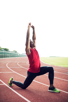 Sportsman kneeling on running track and stretching 
