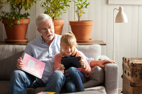 Grandfather and granddaughter (6-7) using digital tablet in living room  