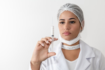 Beautiful young doctor woman in medical white coat and a protective mask and syringe. Isolated over grey background. Copy space for text