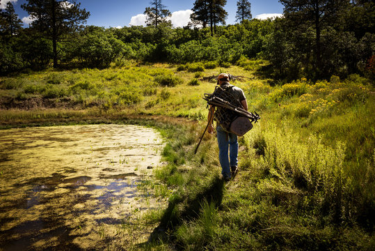 Bow hunter walking past pond 