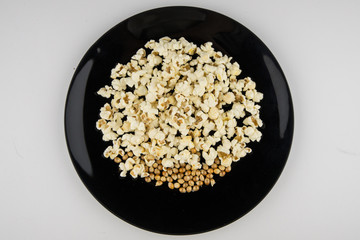 Cooked in the microwave popcorn in a black bowl on a white. unprepared grains remained lying down