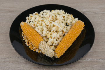 Making popcorn at home in microwave: Well-dried corn on the cob are among grains and the finished product in black plate on white table