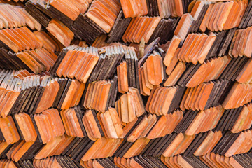 Obraz na płótnie Canvas Abstract piles and packs of a new clay ceramic tiles to cover the roof of a Buddhist temple. Stack of new orange roof tiles in the building construction site for background.