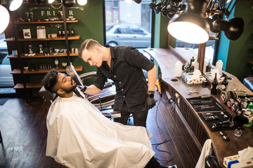Young indian man with beard client in barbershop hairdresser Barber on shaving electric razor