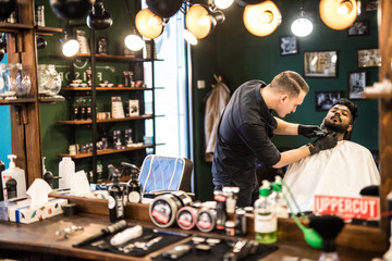 Barber shaving the beard of a handsome bearded man with an electric razor at the barber shop