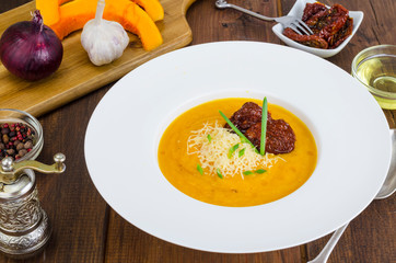 Plate with pumpkin crem soup and dried tomatoes on wooden background