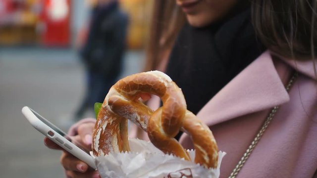 Businesswoman having snack with pretzel while working on cell phone outdoors