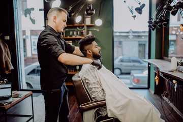 Handsome bearded man is smiling while having his hair cut by hairdresser at the barbershop. Barber shop.