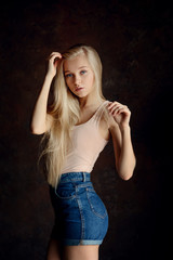 woman with long blonde hair in dark clothes posing in half a turn on the dark background in studio with narural soft light