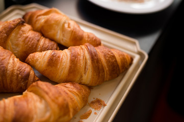 Many large croissants are placed on a light brown tray.