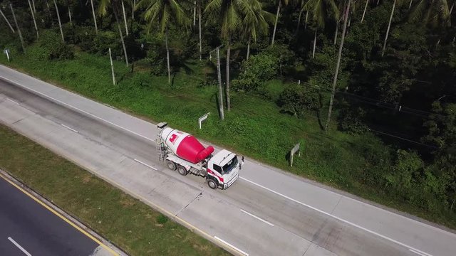 Aerial View of Cement Mixing Truck Driving on Road among Palm Tree Plantation. Cinematic Drone Shot Flying over Concrete Mixing Car Moving in Tropical Country