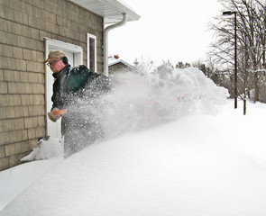 Snow flies from young mans shovel as he removes deep snow from sidewalk after winter snow storm in Minnesota.