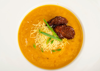 White plate with yellow vegetable cream soup with cheese and dried tomatoes.