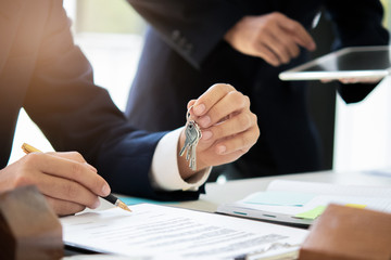 Close up real estate agent holding house key to his client during sign contract agreement in office, concept for real estate, moving home or renting property