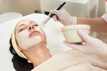 Cosmetologist applying peeling mask on face of her female client