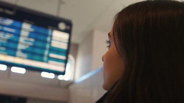 Woman looking at airport display board, checking departure flight status closeup