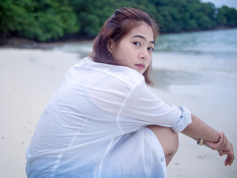 Asian girl looking over shoulder while sitting relaxed on tropical beach. Portrait of happiness young woman smiling at sea Thailand. sweet smile. Bright tone