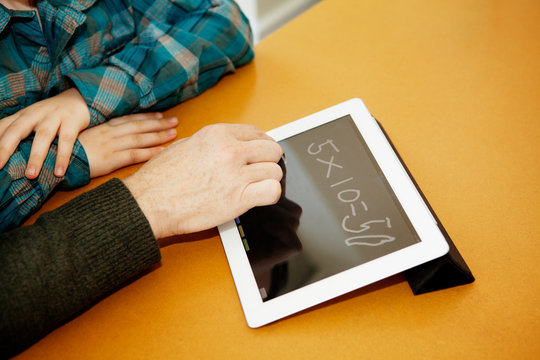 Father and son (8-9) using tablet to teach math 