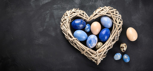 Easter eggs in heart shaped nest on black background.