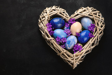 Easter eggs in heart shaped nest on black background.