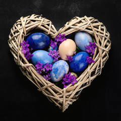 Easter eggs in heart shaped nest on black background.