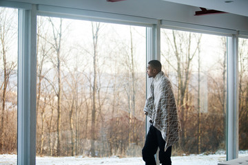 Young man standing by window in living room 