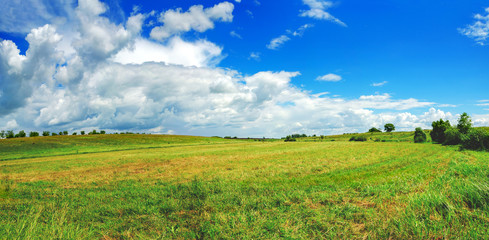 Sunny summer panorama of wide green meadow and beautiful clouds in blue sky