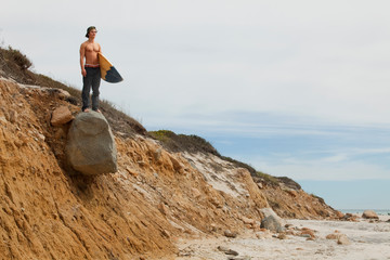 Surfer standing on rocky bluff watching surf