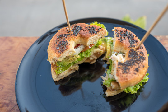 Begel black sesame with chicken salad cut in half with stick on top in black plate.