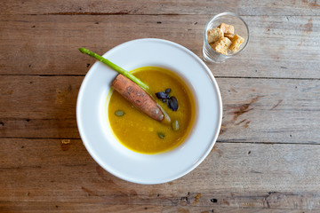 Pumpkin soup with seed and cinnamon stick in white round bowl on wooden table.