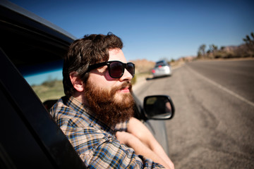 Bearded man in sunglasses looking out through car window road in background 