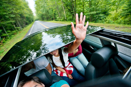 Teen Girl Waving Hand Out Of Sun Roof Of Car 