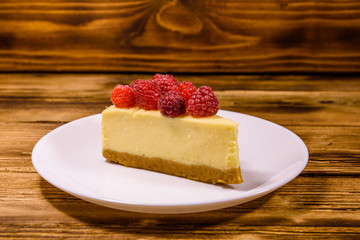 White plate with cheesecake New York and raspberries on wooden table