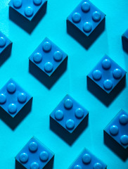 Blue unicolour plastic geometric cubes. Construction toys on geometric shapes paper multi colored background. Arranged in rows.