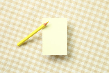 Yellow memo note pad and yellow colored pencil on beige check pattern fabric background
