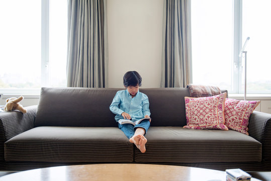 Boy reading book on sofa 